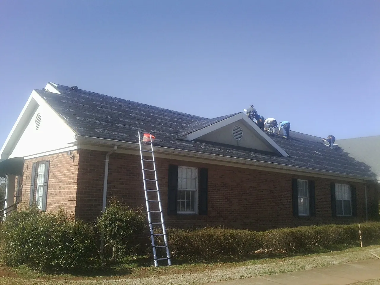 Crew tearing shingles off a brick ranch roof with a ladder set — Metal Roof Repair work by our crew in Fountain City