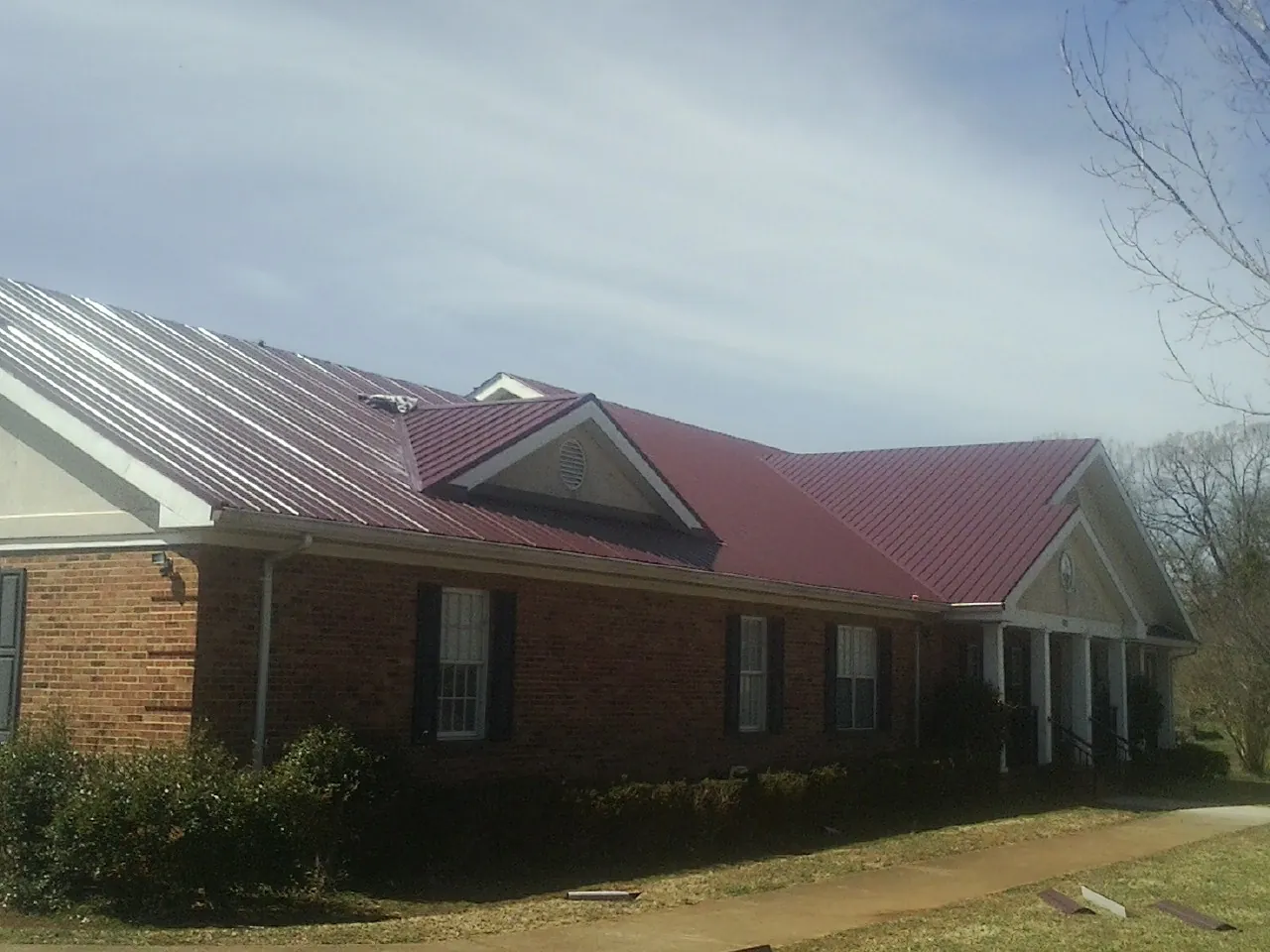 Red metal roof with gabled entries on a long brick building, from a Hail Damage Roof Repair job in Fountain City
