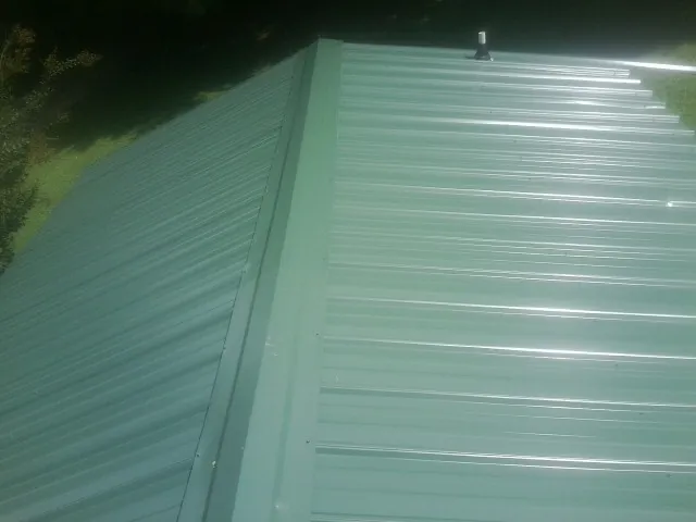 New green metal panels meeting at the ridge of a roof — Flat Roof Repair work by our crew in Fountain City
