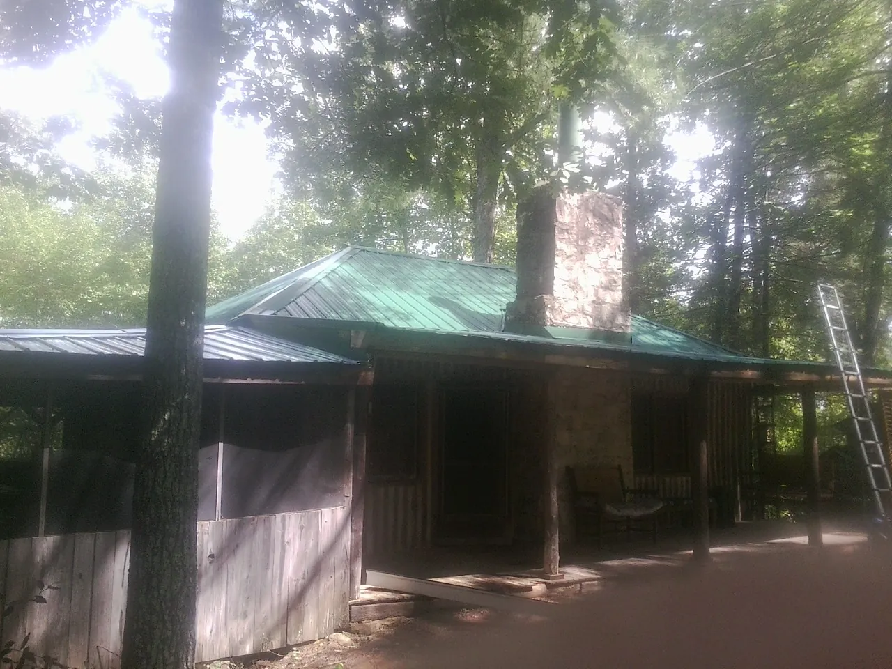 Green metal roof and stone chimney above a log cabin porch in Fountain City