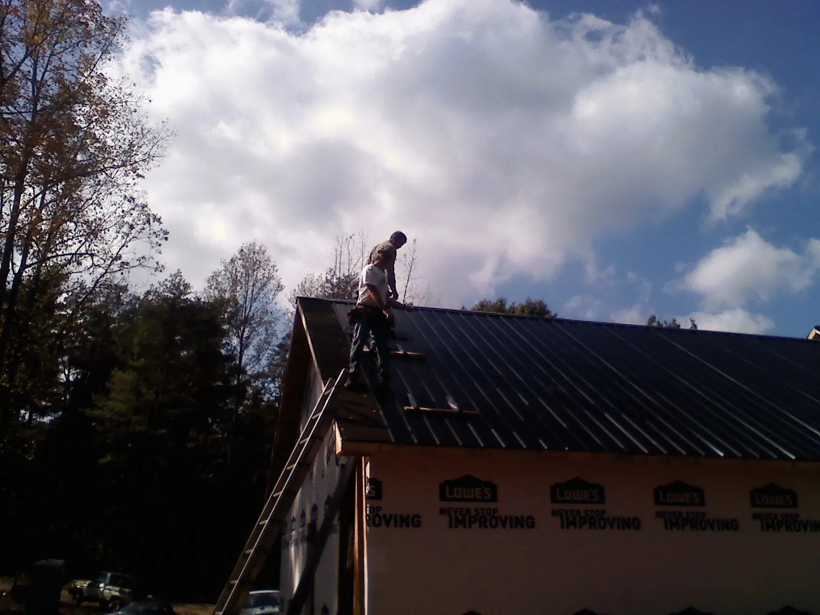 Roofer fastening dark metal panels high against a cloudy sky, from a Roof Inspection job in Fountain City