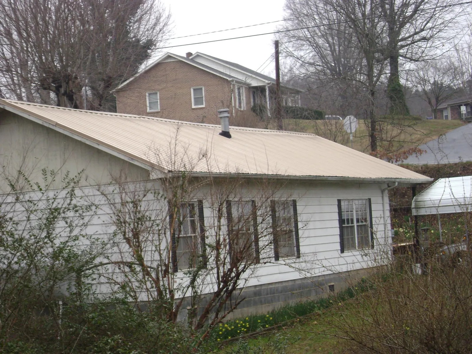 Tan metal roof on a white sided house set into a hillside — Commercial Roofing by Roofing Brothers in Fountain City